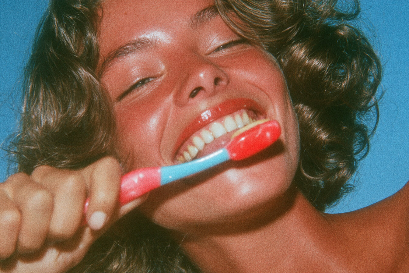 Blonde woman smiling while brushing her teeth in a bathroom mirror selfie